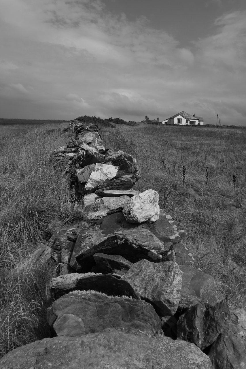 Dry Stone. A stone wall leading across the field to a white house.