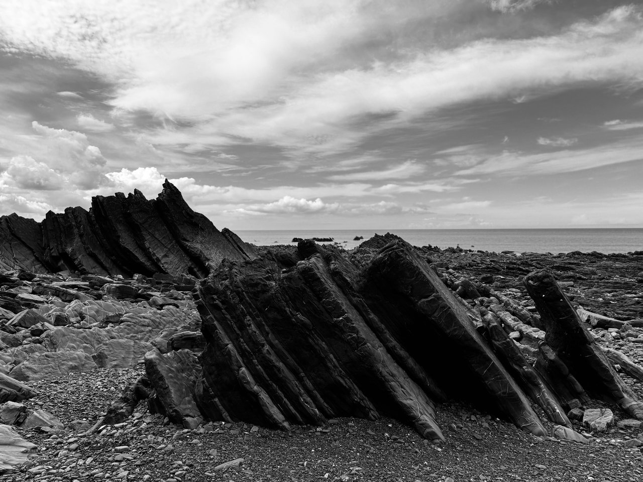 Ridges. Tilted rock ridges on the shore under a wide sky.