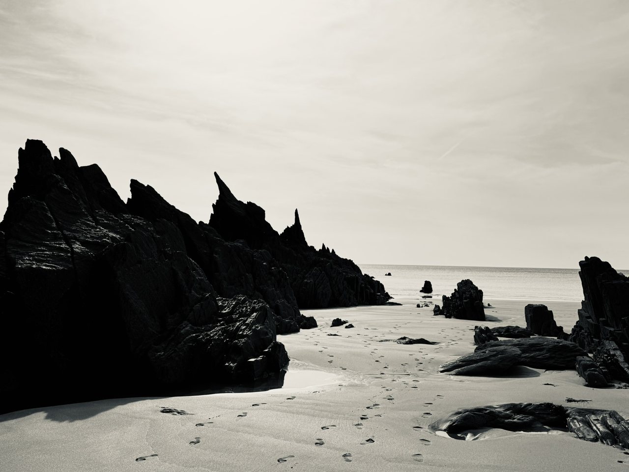 Spires. Black rock against a white sky, footprints leading out to the sea.